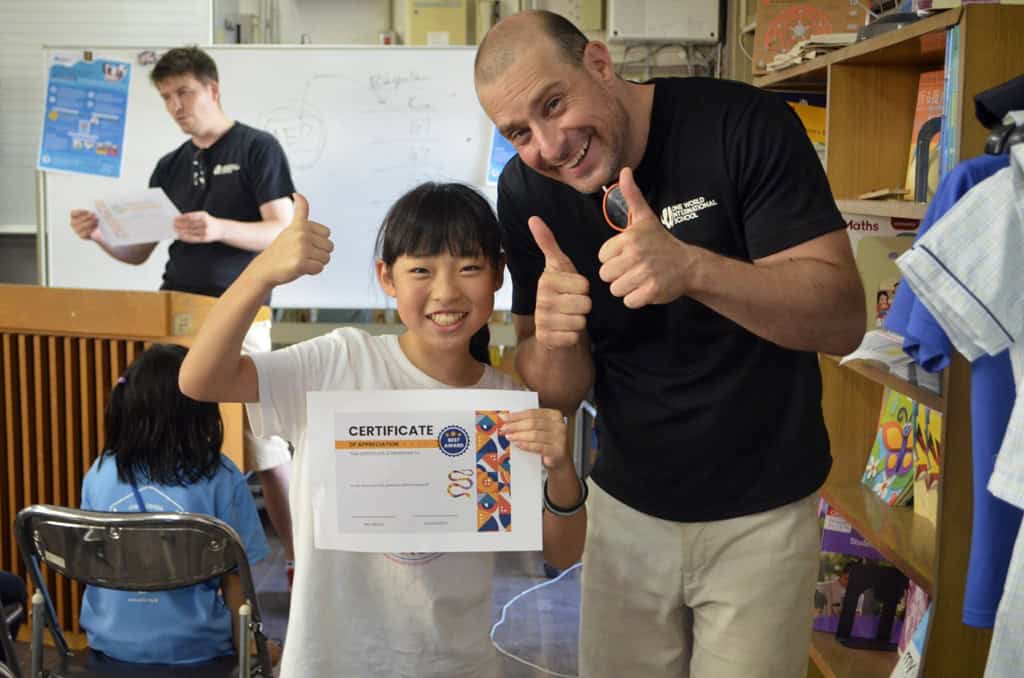 Mission, certification - One World International School Teacher teacher holding thumbs up and smiling with a student who was awarded a certificate